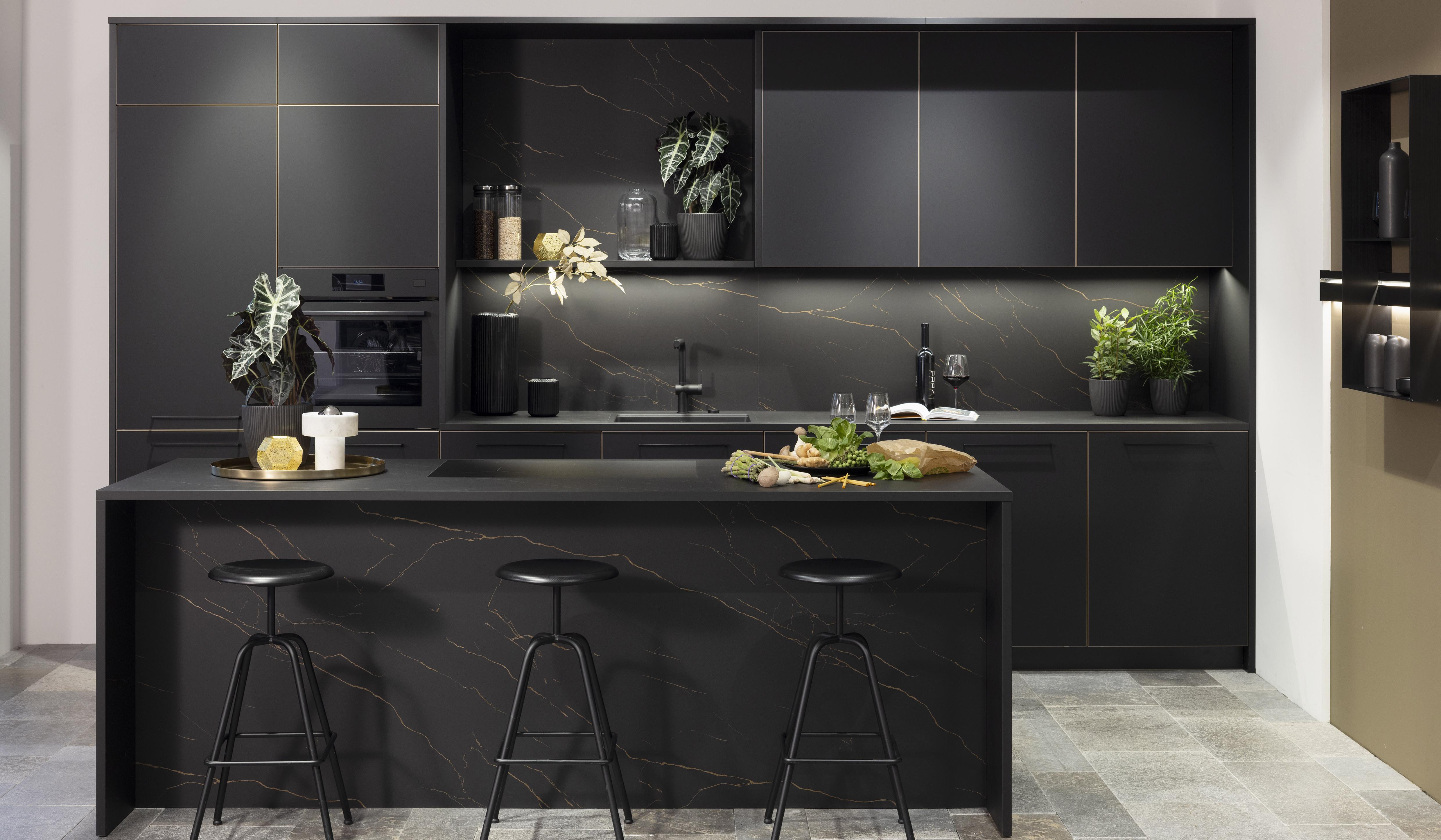 Moderne schwarze Küche mit Insel, Barhockern und grünen Pflanzen.
