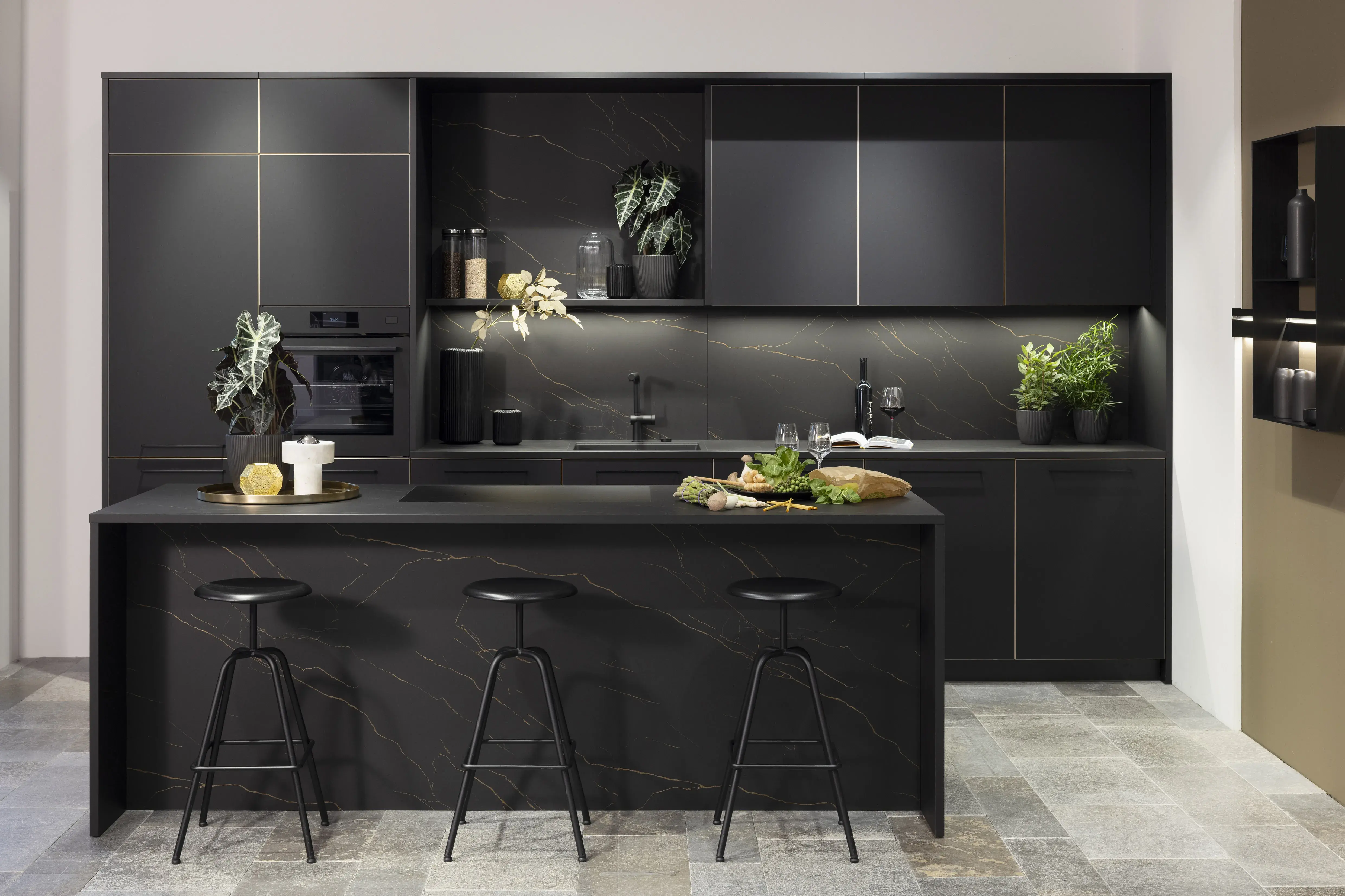 Moderne schwarze Küche mit Insel, Barhockern und grünen Pflanzen.