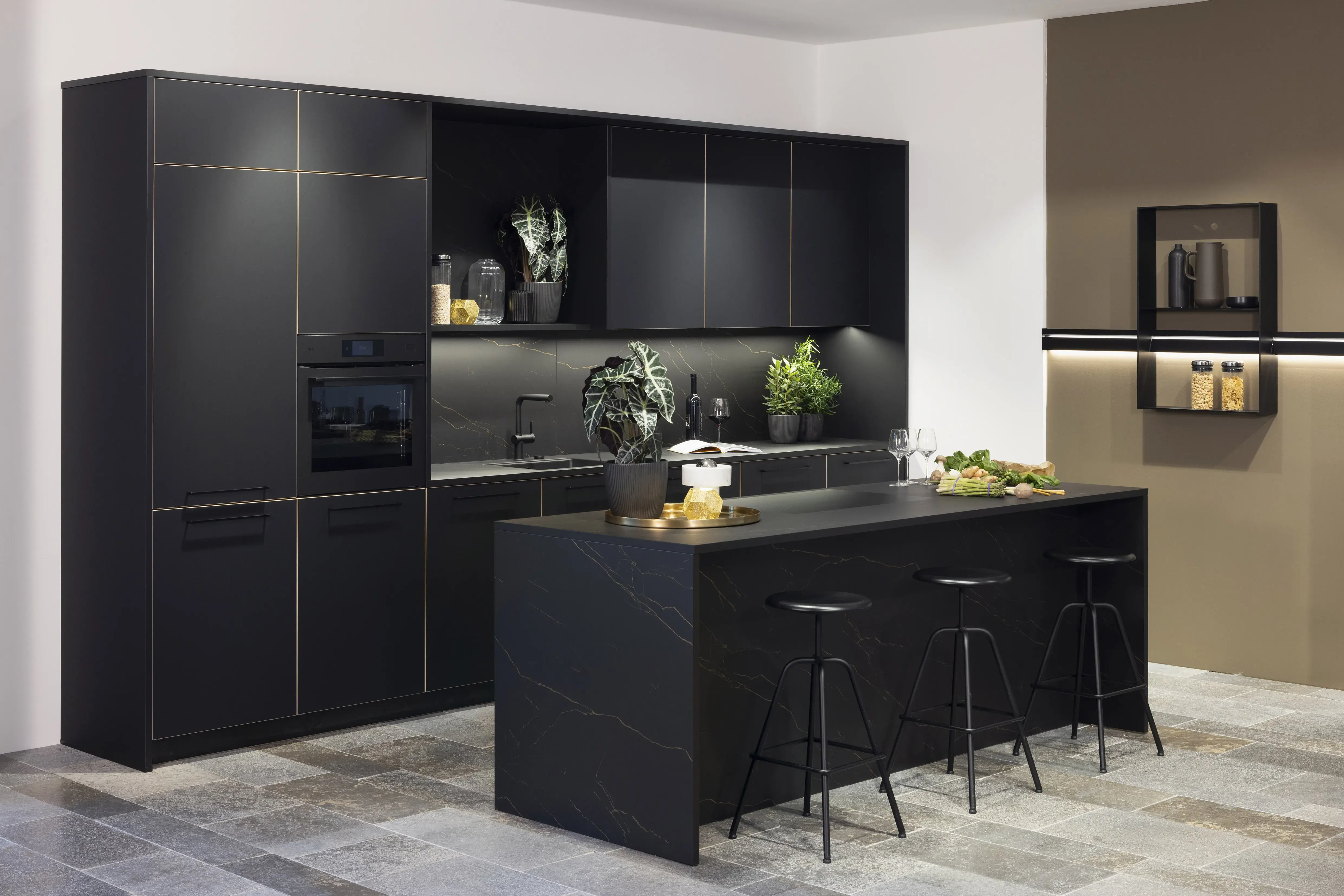 Moderne schwarze Küche mit Kochinsel, Barhockern und grünen Pflanzen.