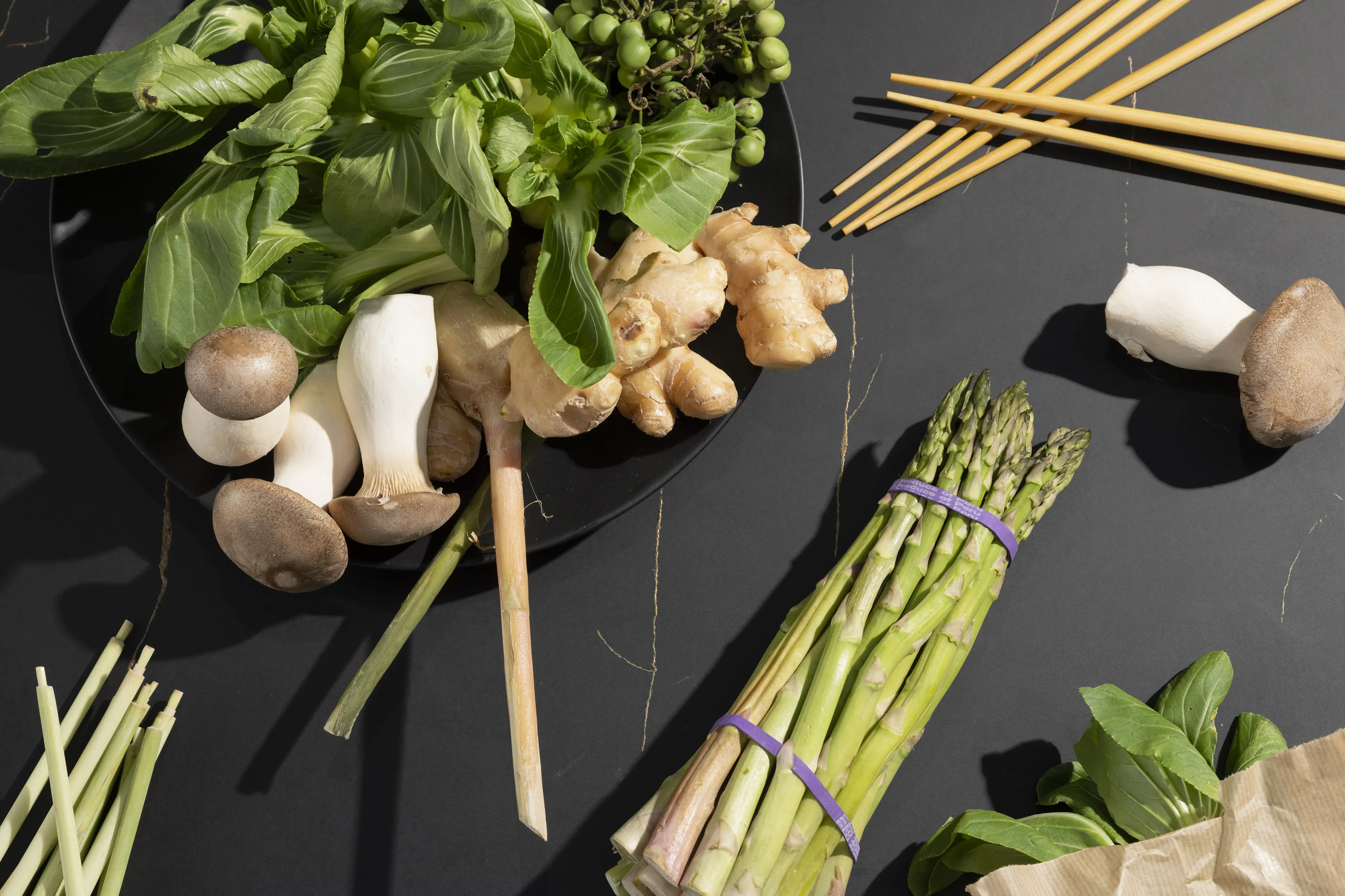 Frisches Gemüse, Kräuter, Spargel, Ingwer und Pilze auf dunklem Untergrund.