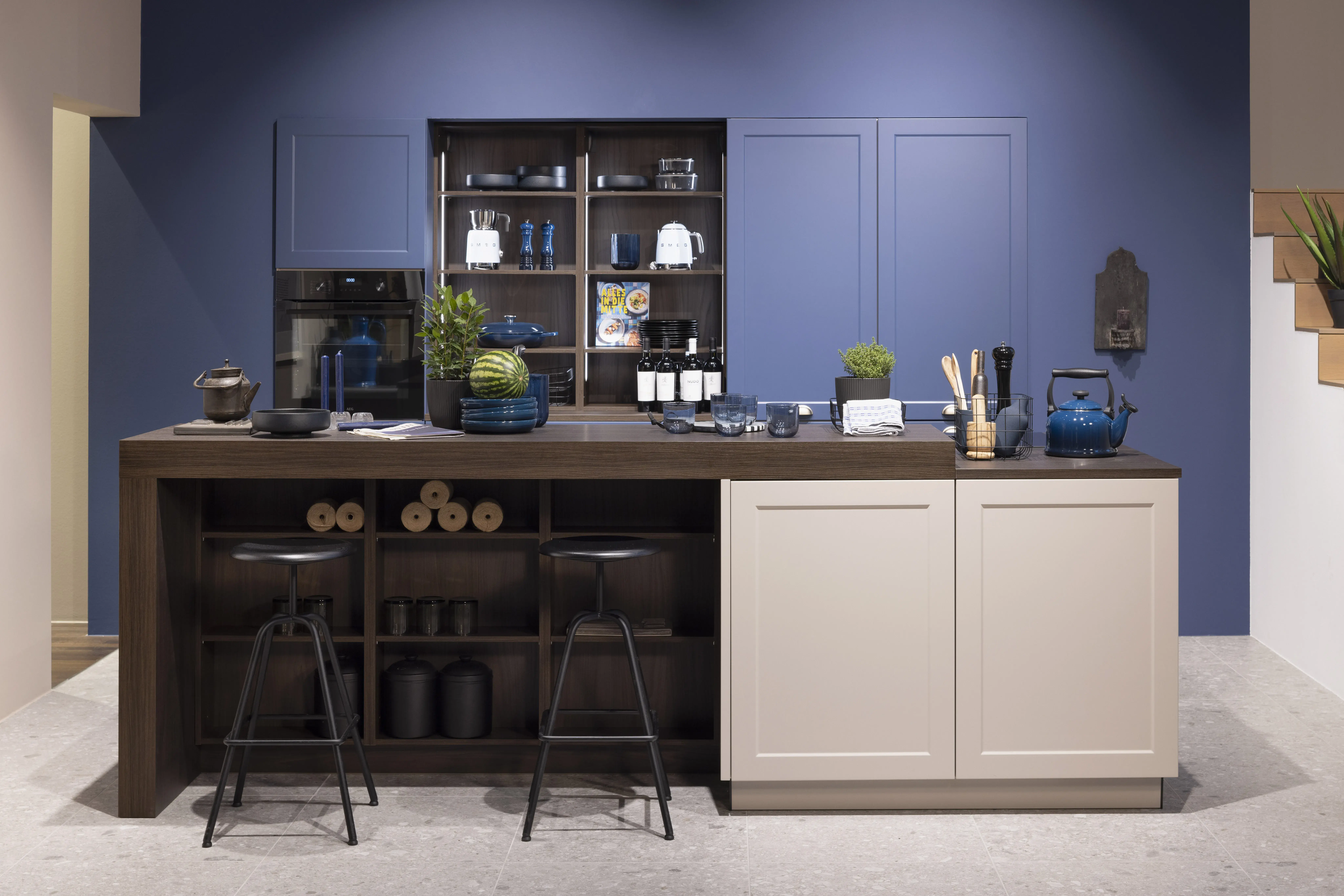 Moderne Küche mit Kochinsel, blauer Wand und Regalen, zwei schwarze Hocker davor.